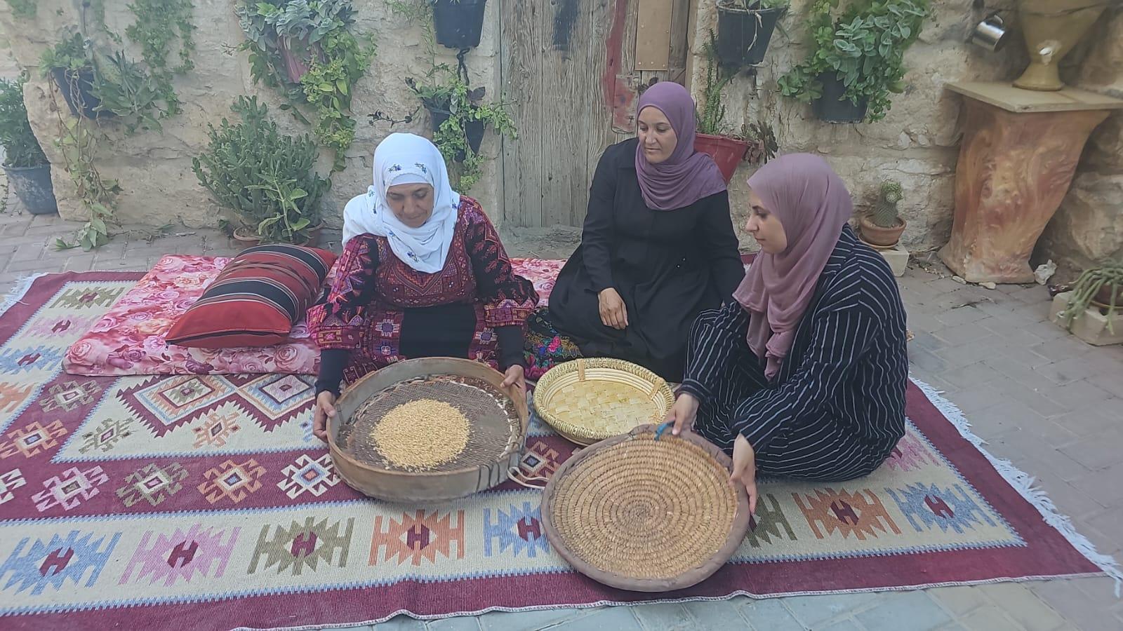 Three women demonstrating traditional wheat-sifting for a heritage story