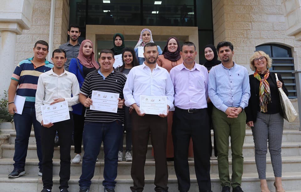 Participants holding certificates on the steps after a training